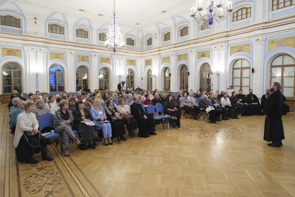 Архимандрит Савва (Мажуко) выступает перед аудиторией в просторном зале с высокими окнами и люстрами
