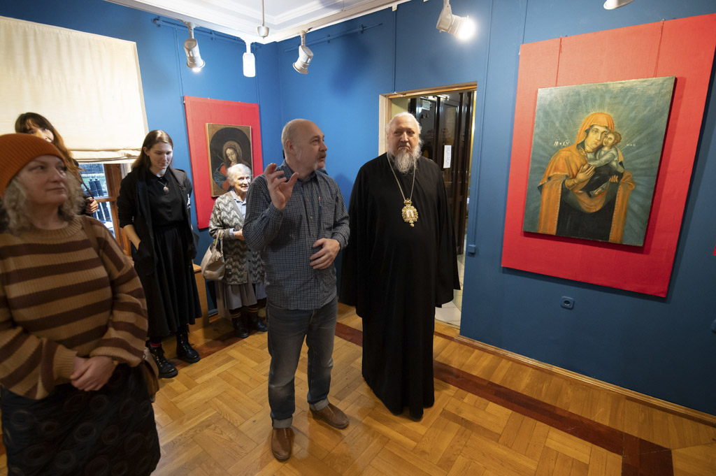 Экскурсовод увлеченно рассказывает о выставке священнику и группе посетителей